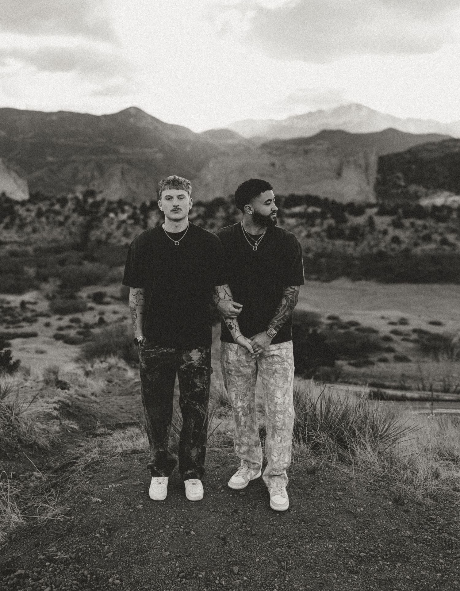 Black and white photograph of two people standing together on a hillside with mountains in the background.