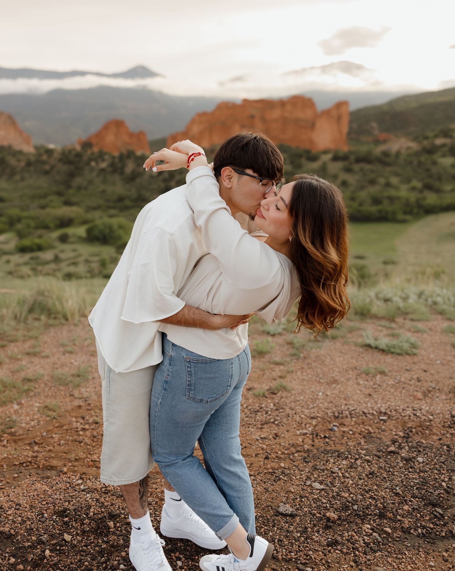 A romantic embrace at the Garden of the Gods in Colorado with red rock formations and mountains in the background.