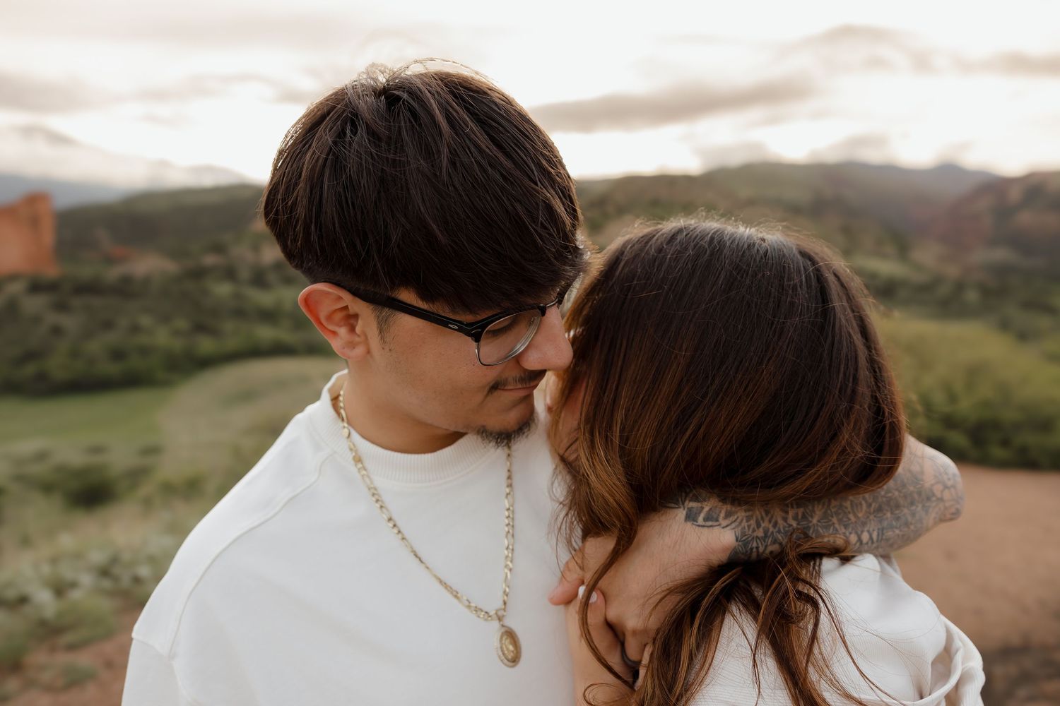 A romantic couple embraces while sharing an intimate moment together against a scenic mountain landscape at sunset.