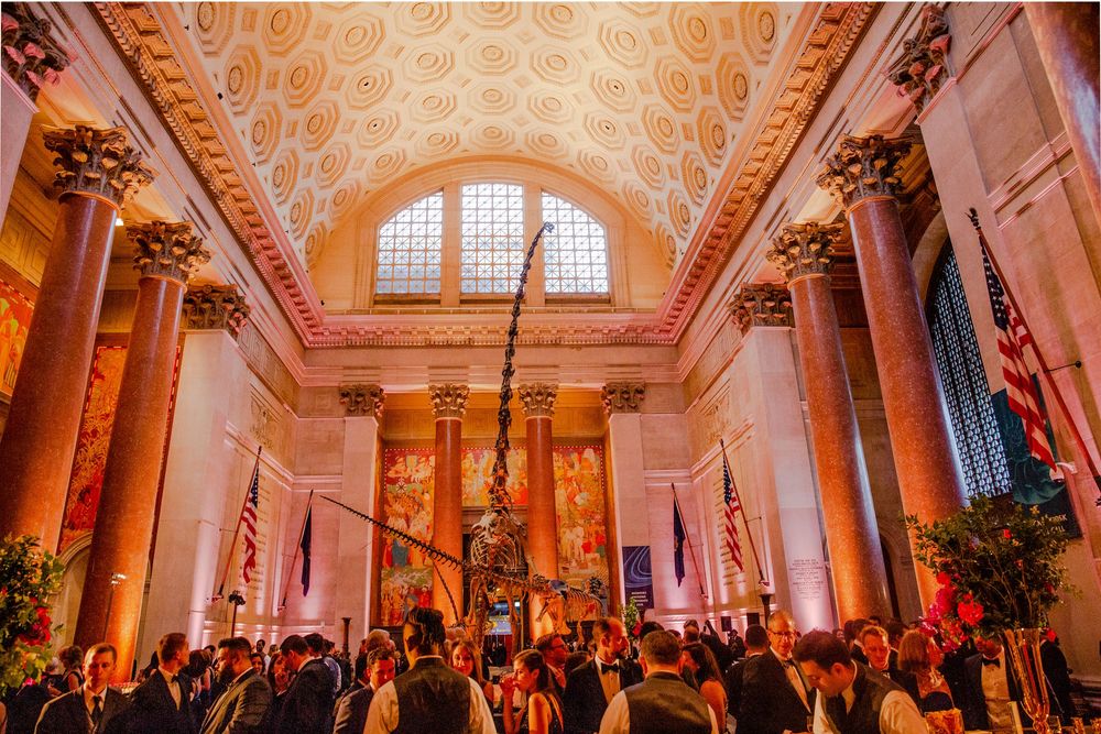Elegant grand hall with ornate ceiling and columns filled with guests at an upscale evening event.
