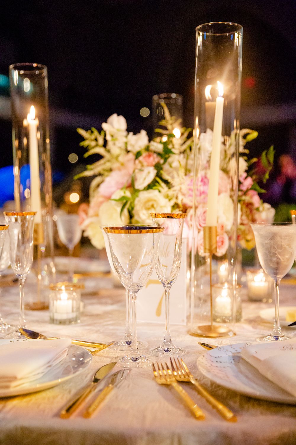 Elegant table setting with tall candle holders, crystal glasses and pink floral centerpiece for an upscale wedding reception.