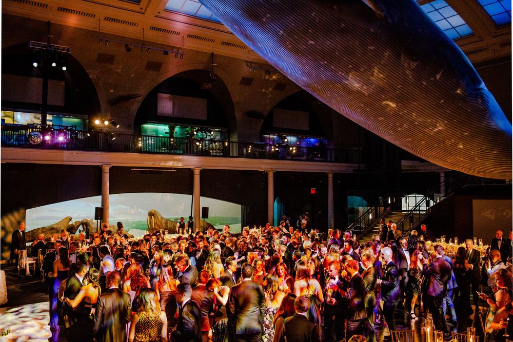 A crowded dance floor filled with party guests under dramatic lighting at an indoor venue.