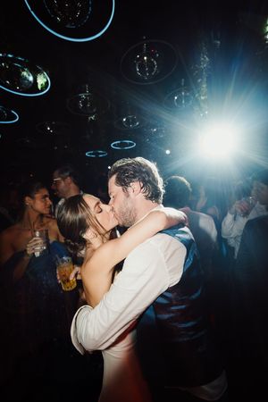 A couple shares a romantic dance and kiss on a dimly lit dance floor with bubble-like decorations floating above.