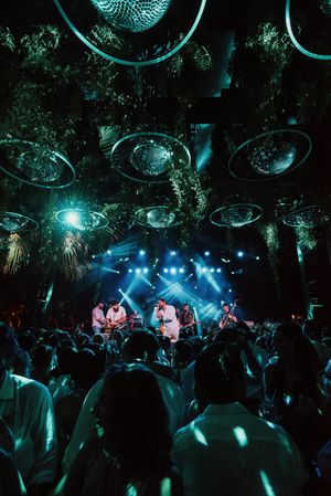Energetic nightclub scene with disco balls and blue lighting illuminating a crowded dance floor during a live performance.