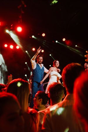 A performer in a blue vest on stage under dramatic red lighting and spotlights during a concert performance.
