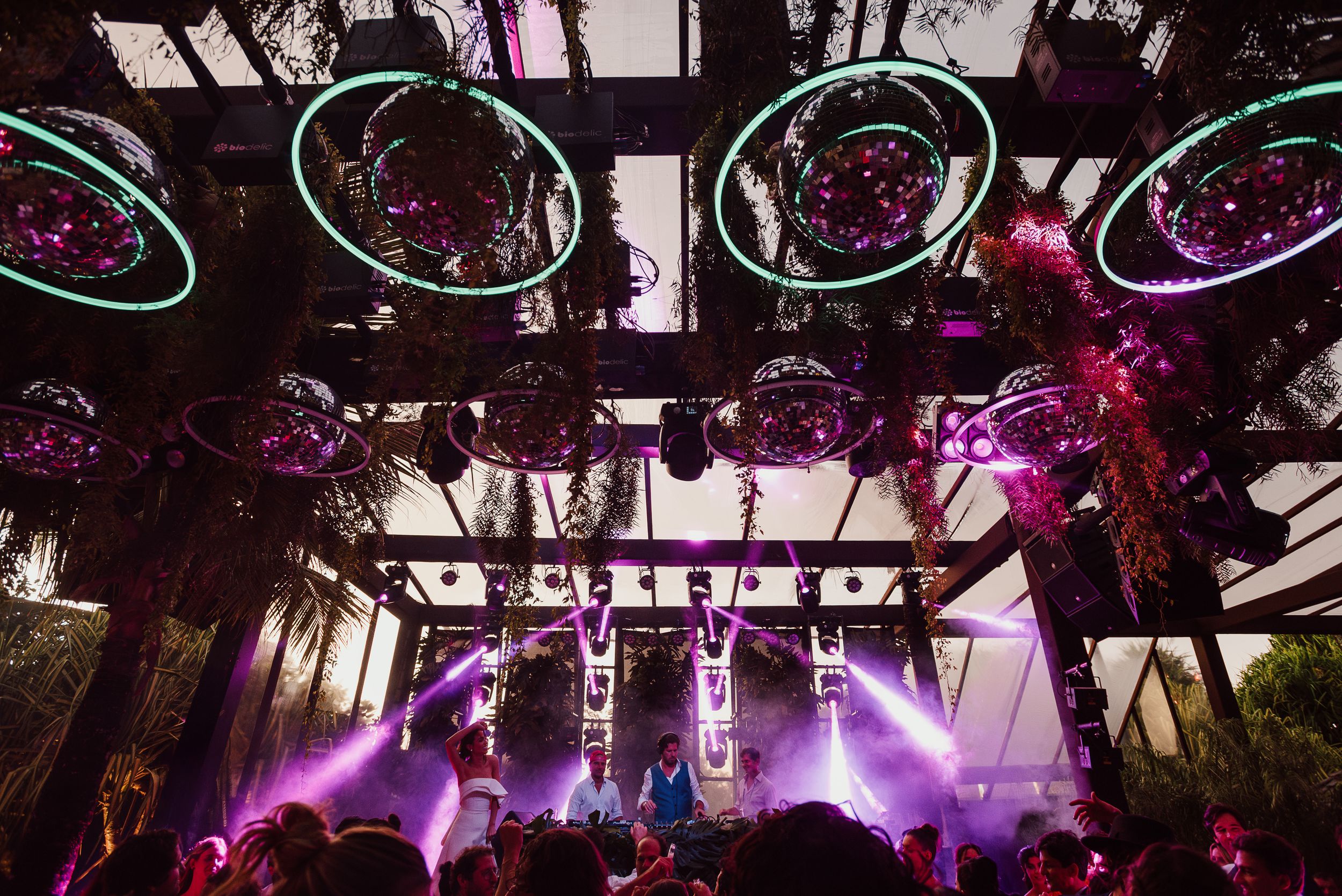 Concert stage with dramatic purple lighting and circular overhead fixtures creating an atmospheric outdoor performance setup.
