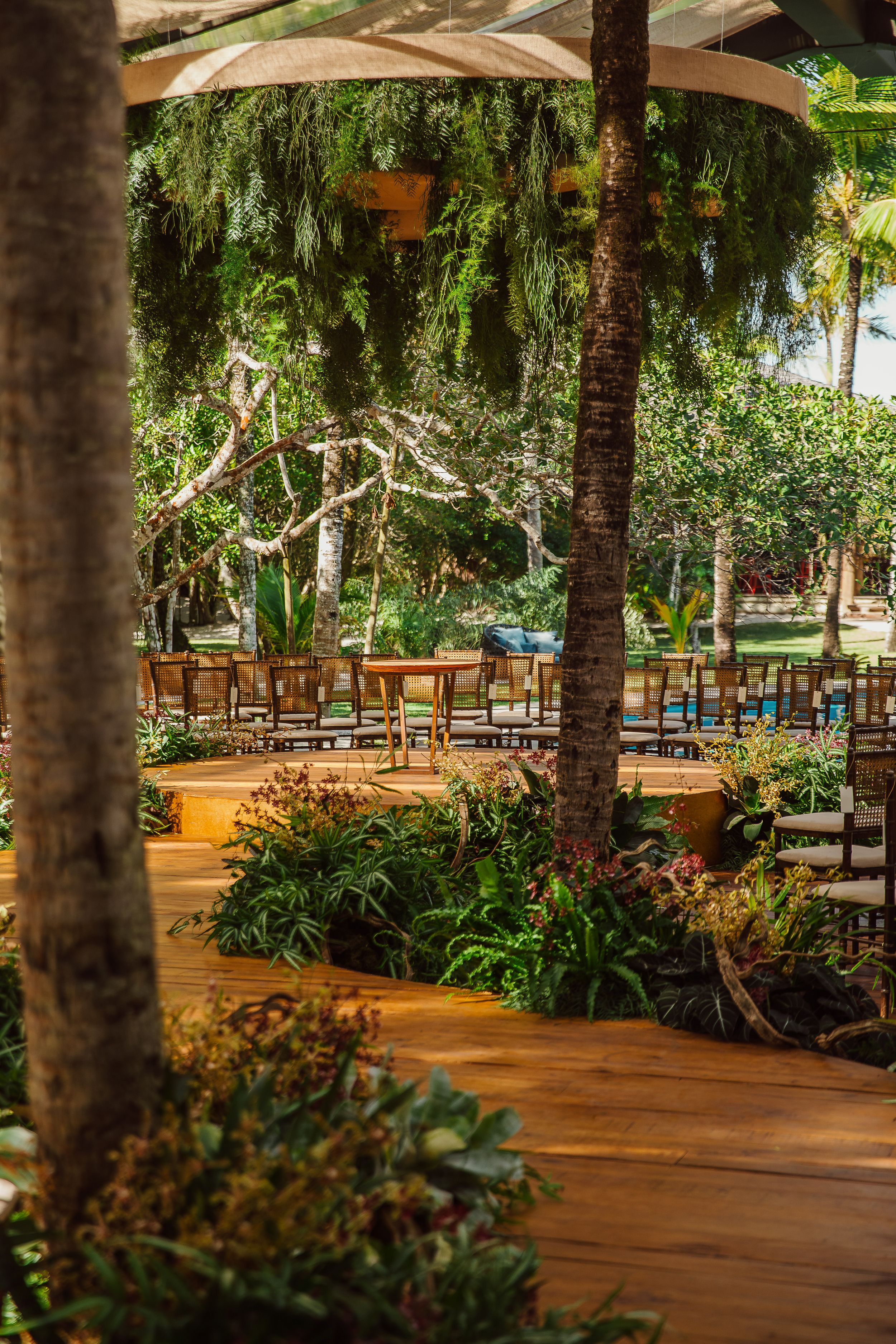 Wooden deck outdoor dining area with lush tropical plants, weeping willows and string lights creating a romantic ambiance.