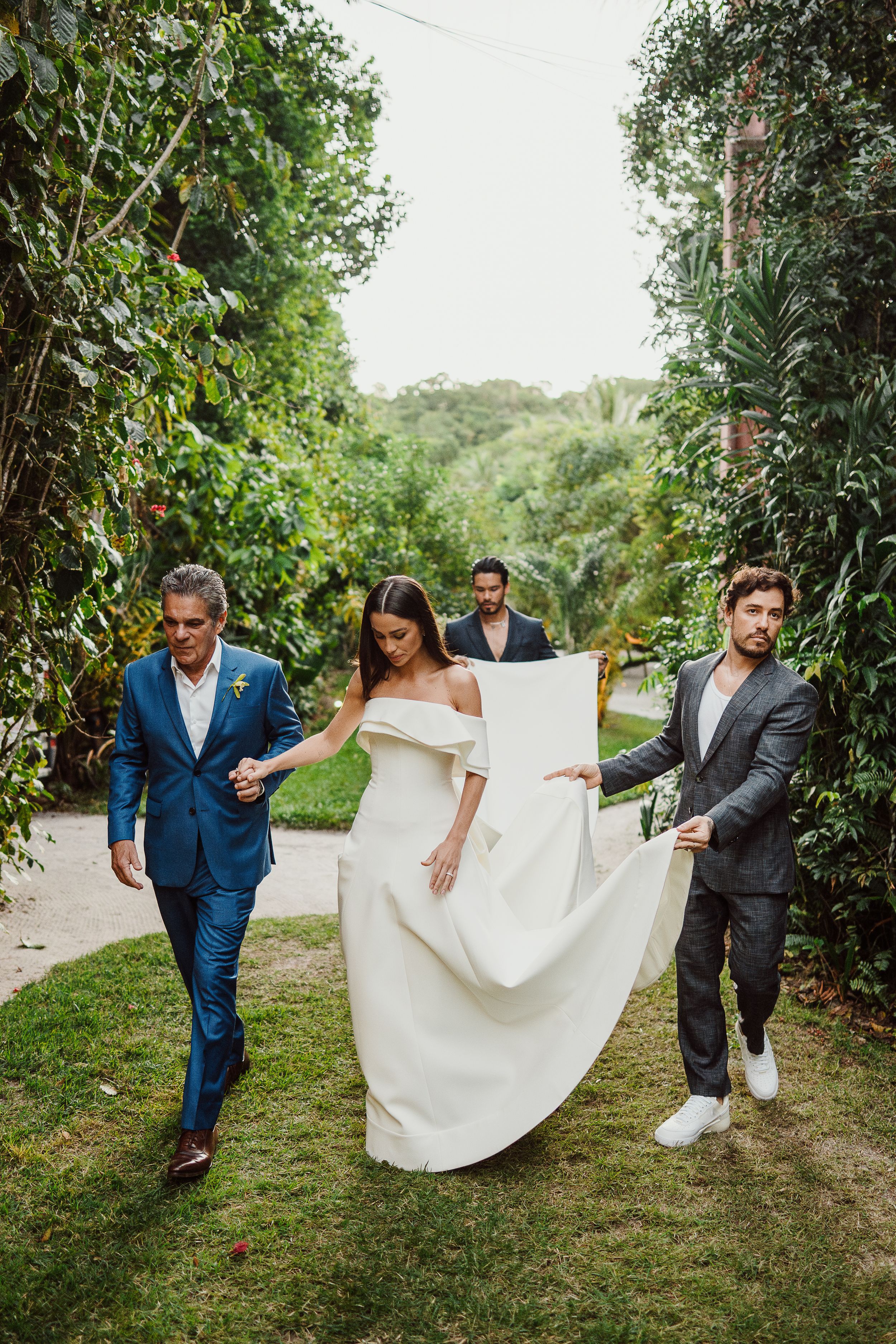 A wedding party walks along a lush garden path with vibrant greenery creating a natural corridor.
