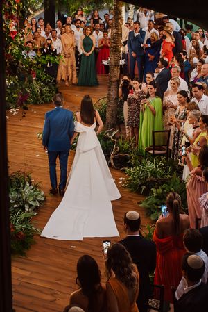 A couple walks down a wooden aisle during an outdoor wedding ceremony surrounded by guests and floral decorations.