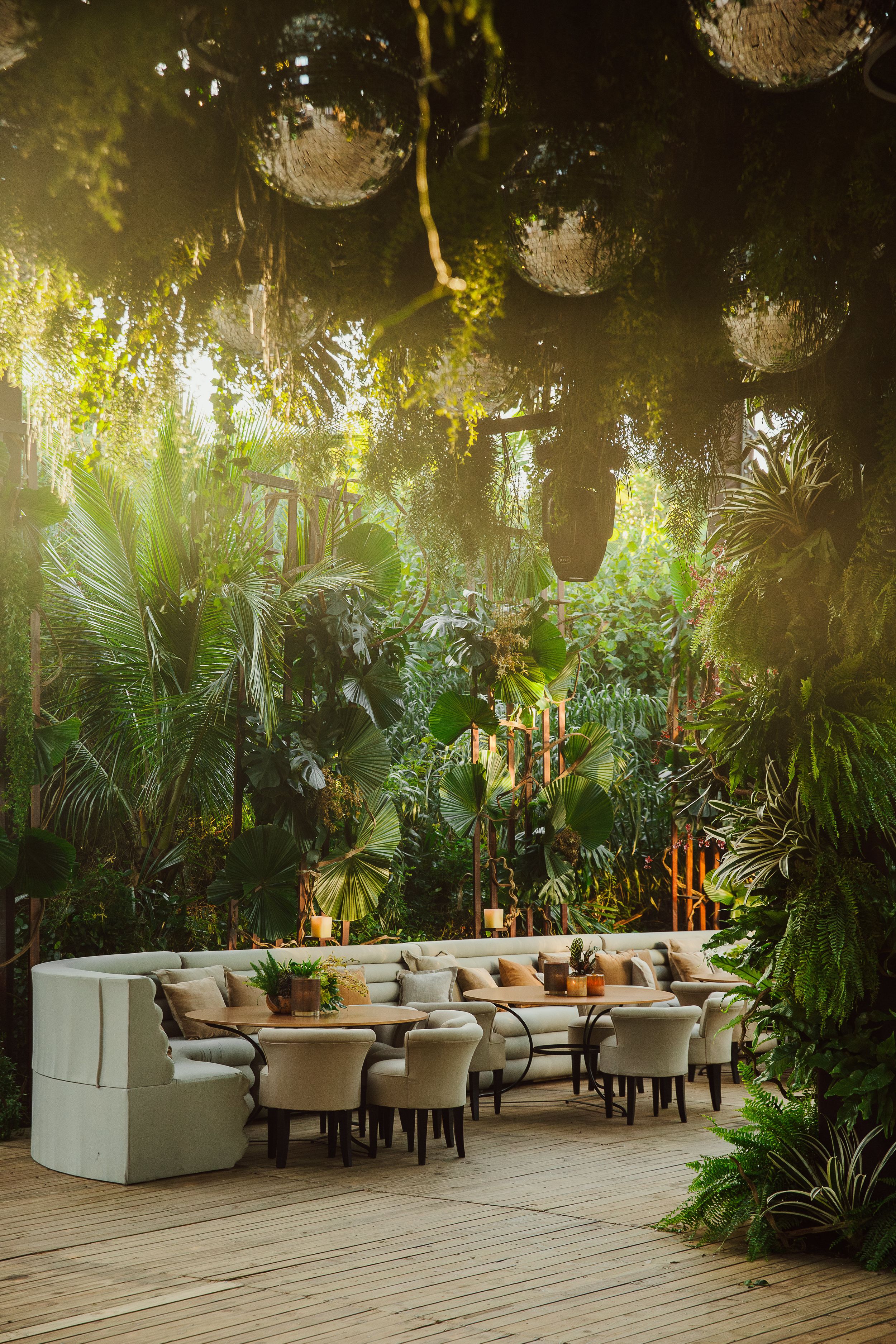 Luxurious outdoor restaurant seating area surrounded by tropical plants and hanging disco balls creating magical ambiance.