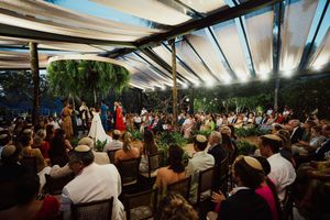 Wedding ceremony under a covered outdoor pavilion with guests seated in rows during a garden celebration.