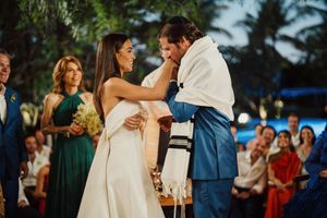 A joyous couple dances together during a traditional Jewish wedding celebration outdoors at sunset.