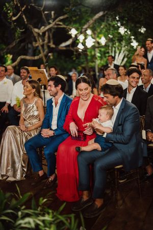 Wedding guests share candid laughing moments while seated at an outdoor reception venue in a garden setting.