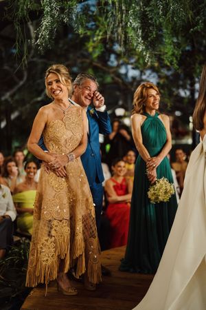 Wedding ceremony guests smile and laugh during an outdoor celebration with decorative hanging greenery and elegant formal attire.