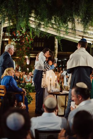 Jewish wedding celebration under hanging willow branches with guests gathered at outdoor reception venue.