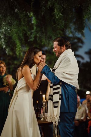 A tender moment during a wedding ceremony at night with candlelight and greenery in the background.