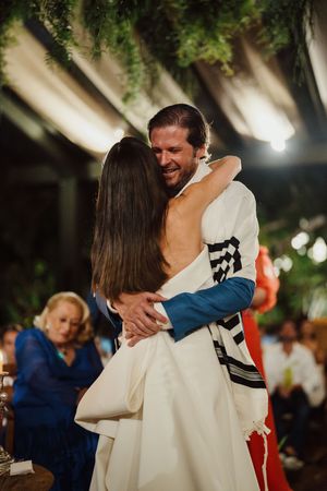 A couple shares an intimate dance embrace at an outdoor wedding celebration under twinkling lights and greenery.