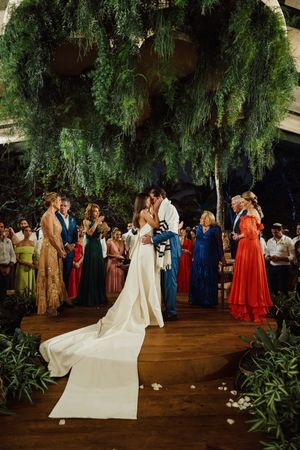 A romantic evening wedding celebration under dramatic weeping willow trees with guests gathered on a wooden dance floor.