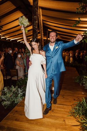 A celebratory moment at a wedding reception with a bride in white dress and groom in blue suit raising their arms in joy.