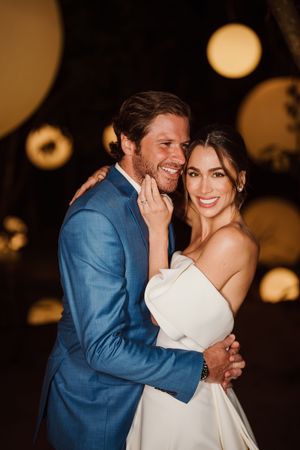 A couple shares a romantic embrace during their wedding reception with warm glowing lights in the background.