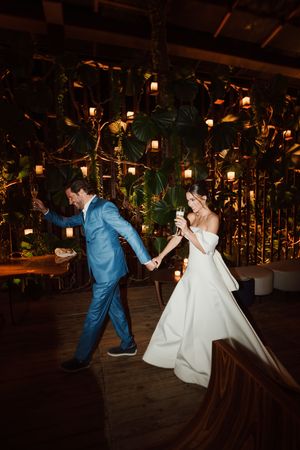 A couple dances together on a wooden floor under hanging lanterns and greenery at an elegant evening reception.