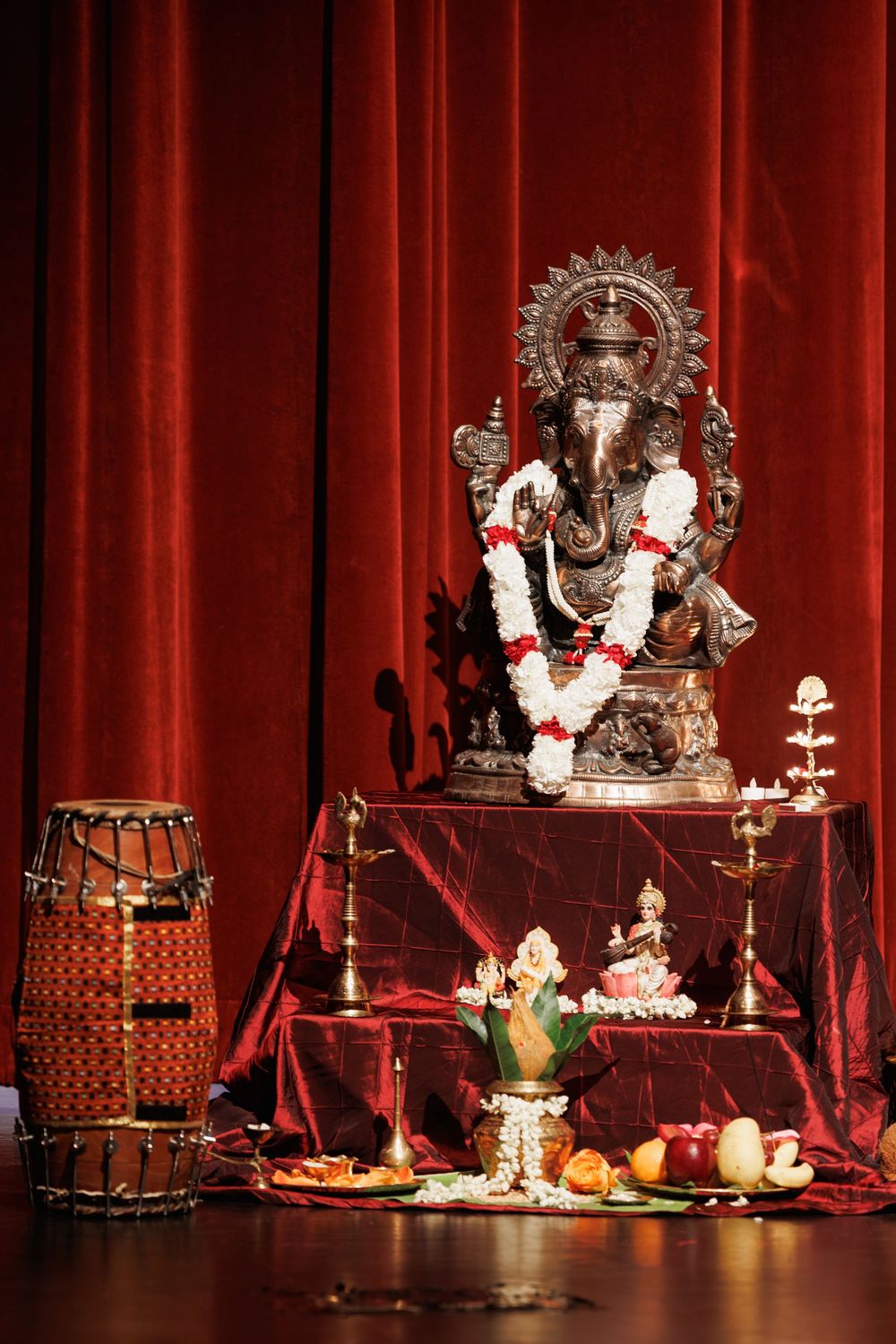 Traditional Indian altar setup with Ganesha statues and decorative items against red curtains.