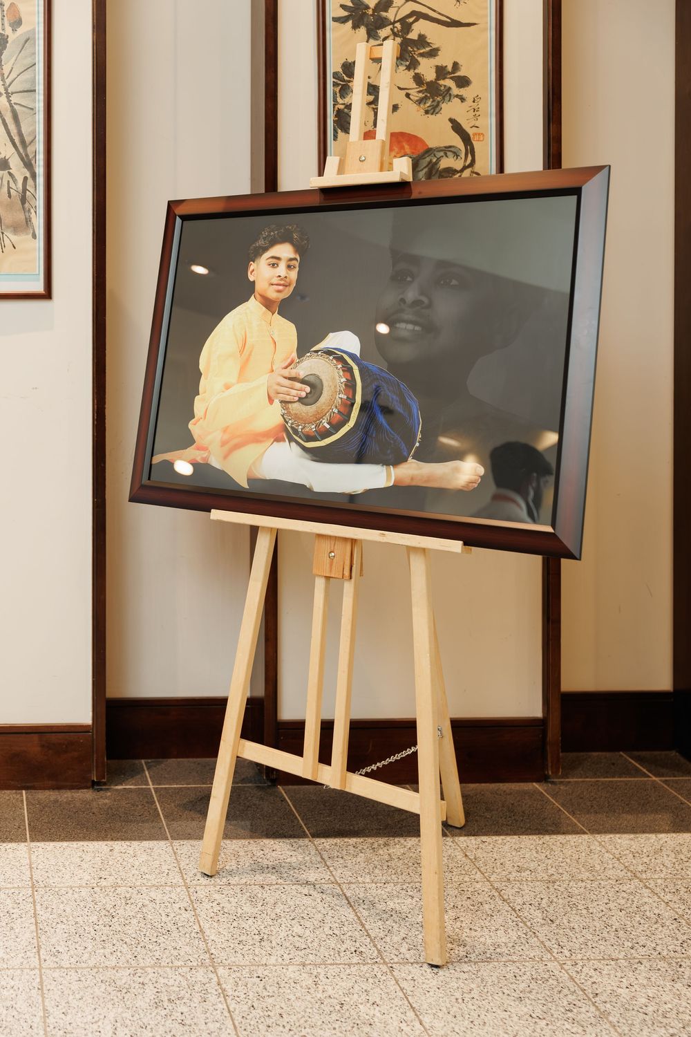 Framed artwork and photographs displayed on wooden easels in a gallery setting.