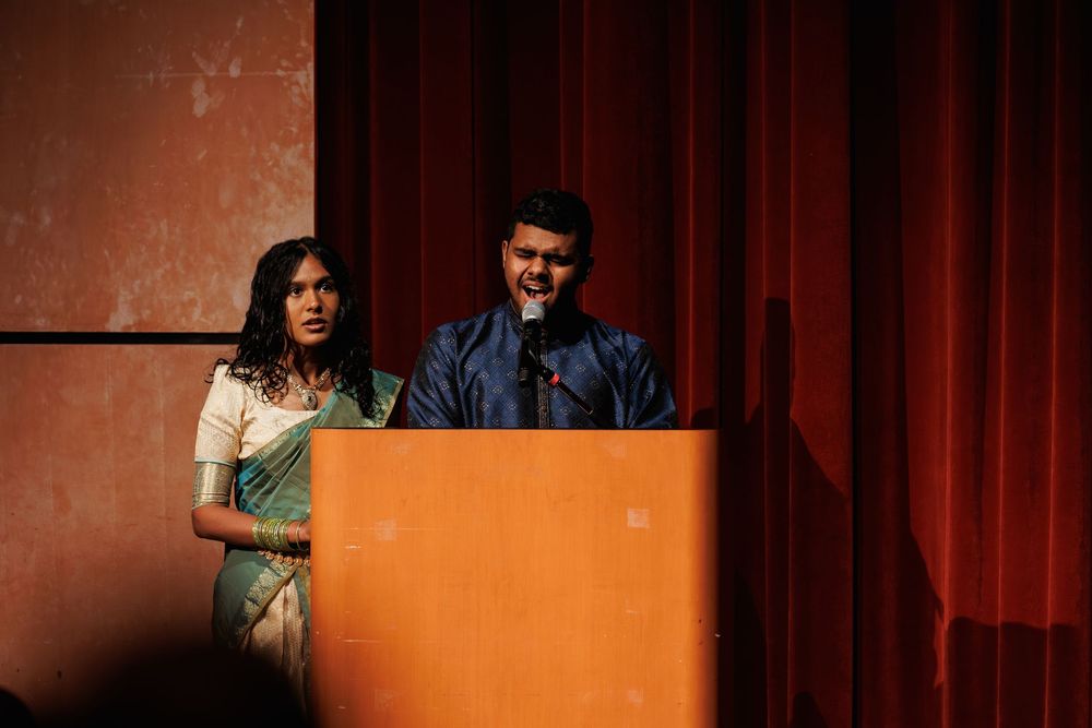 A dramatic stage performance with artistic lighting and orange backdrop creates a theatrical atmosphere.