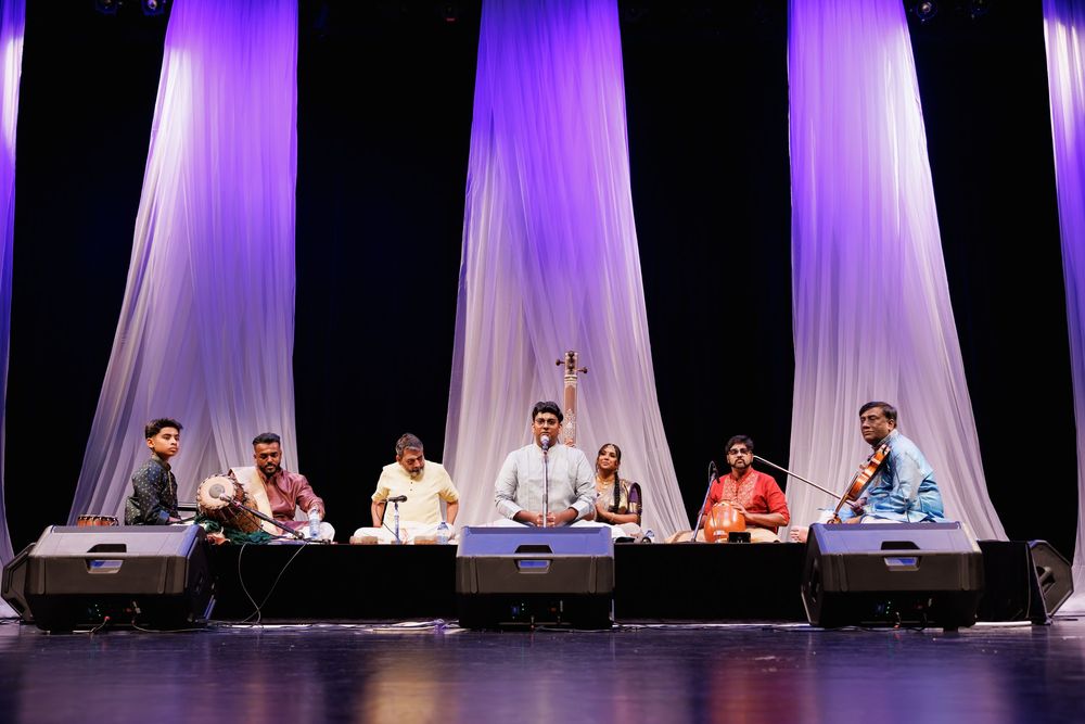 Musicians perform traditional Indian music on stage with purple curtain backdrop during a cultural concert.