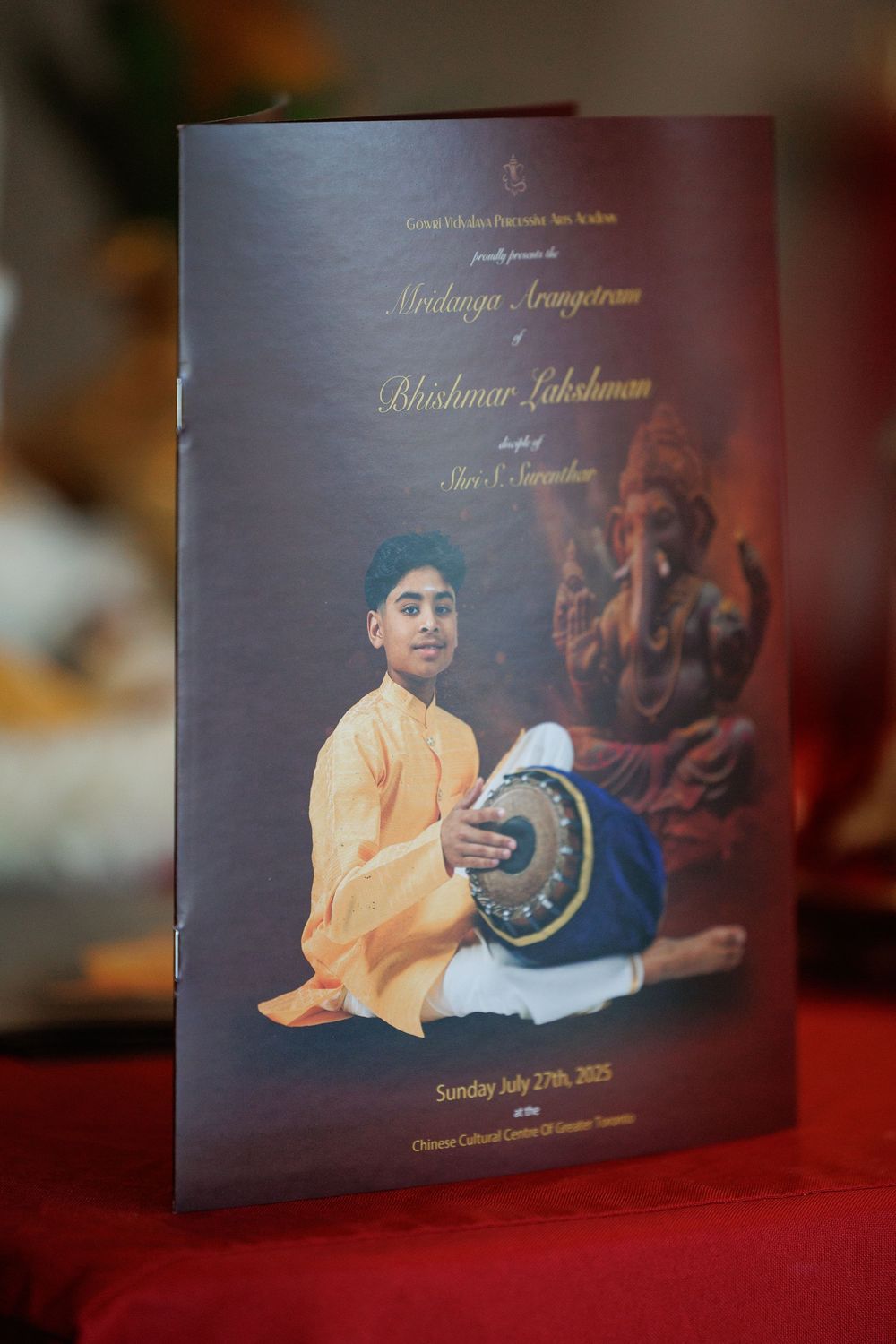 Performance program cards displayed on red cloth featuring traditional Indian music themes.