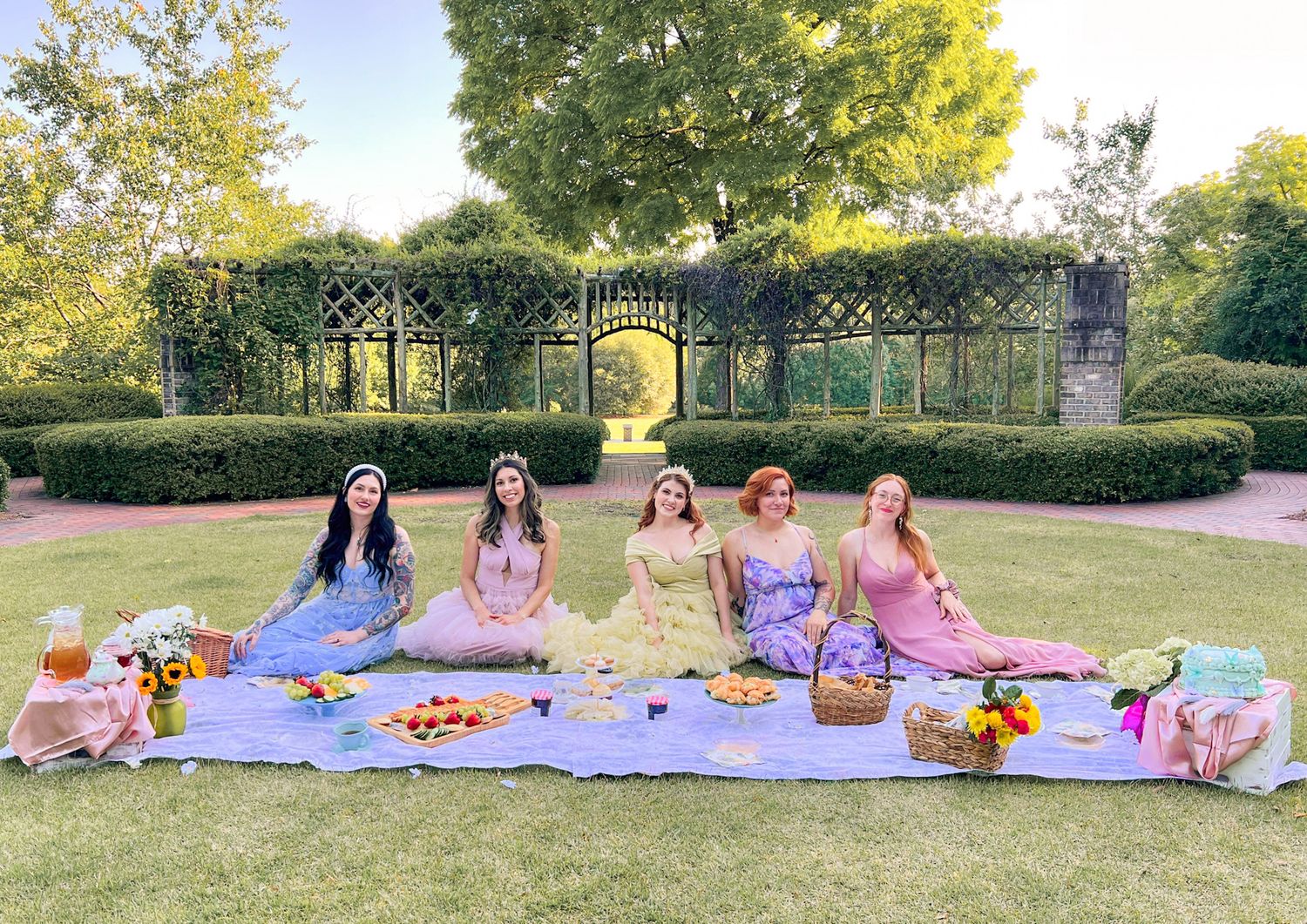 Group enjoying a sunny autumn picnic on blankets spread out in a park with trees and hedges in the background.