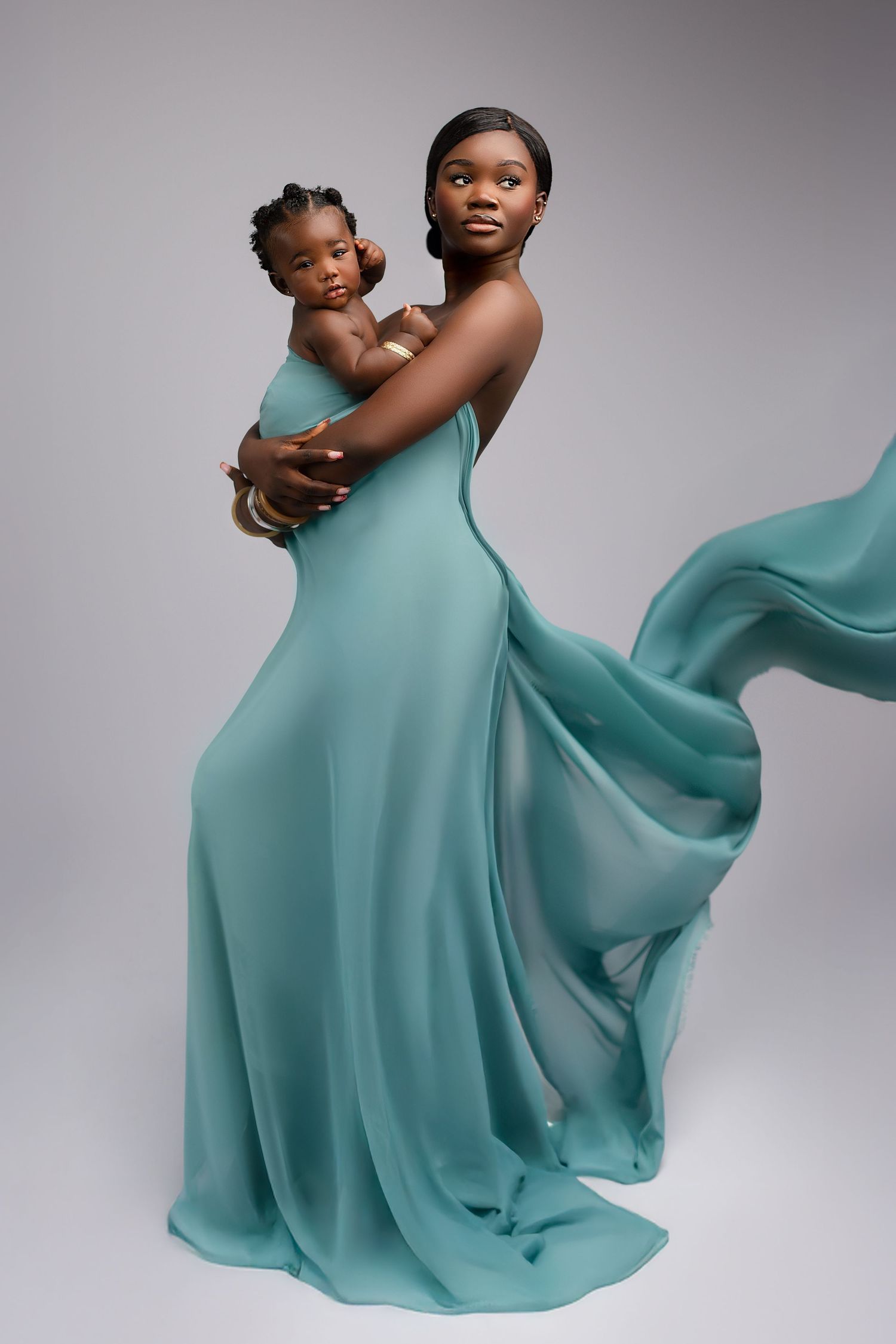 A graceful portrait in a flowing turquoise dress holding a small child against a gray studio backdrop. springdield lakes