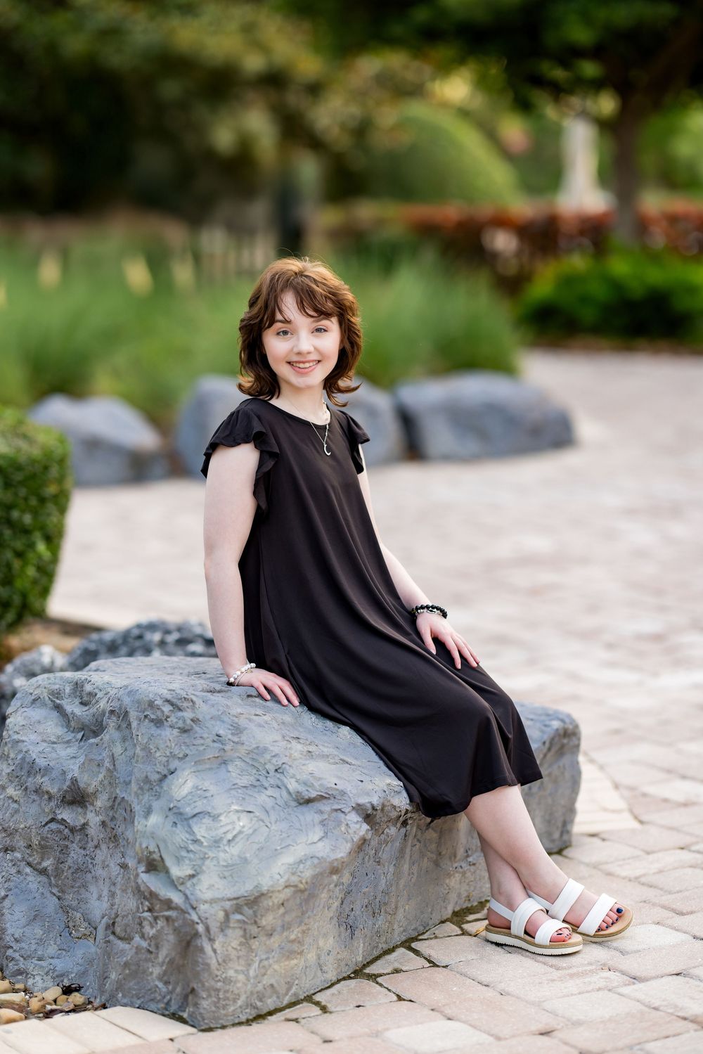 Person in black dress sitting casually on large rock in landscaped garden. Photos by Tampa Photographer DigitalMyst Photography