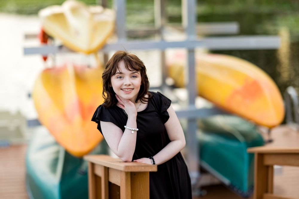 Person in black dress leaning on wooden railing near colorful kayaks. Photos by Tampa Photographer DigitalMyst Photography