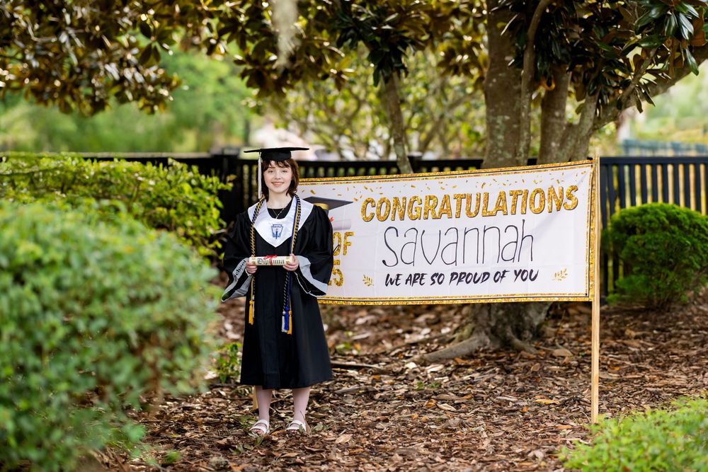Graduation photo in front of congratulatory banner among trees. Photos by Tampa Photographer DigitalMyst Photography