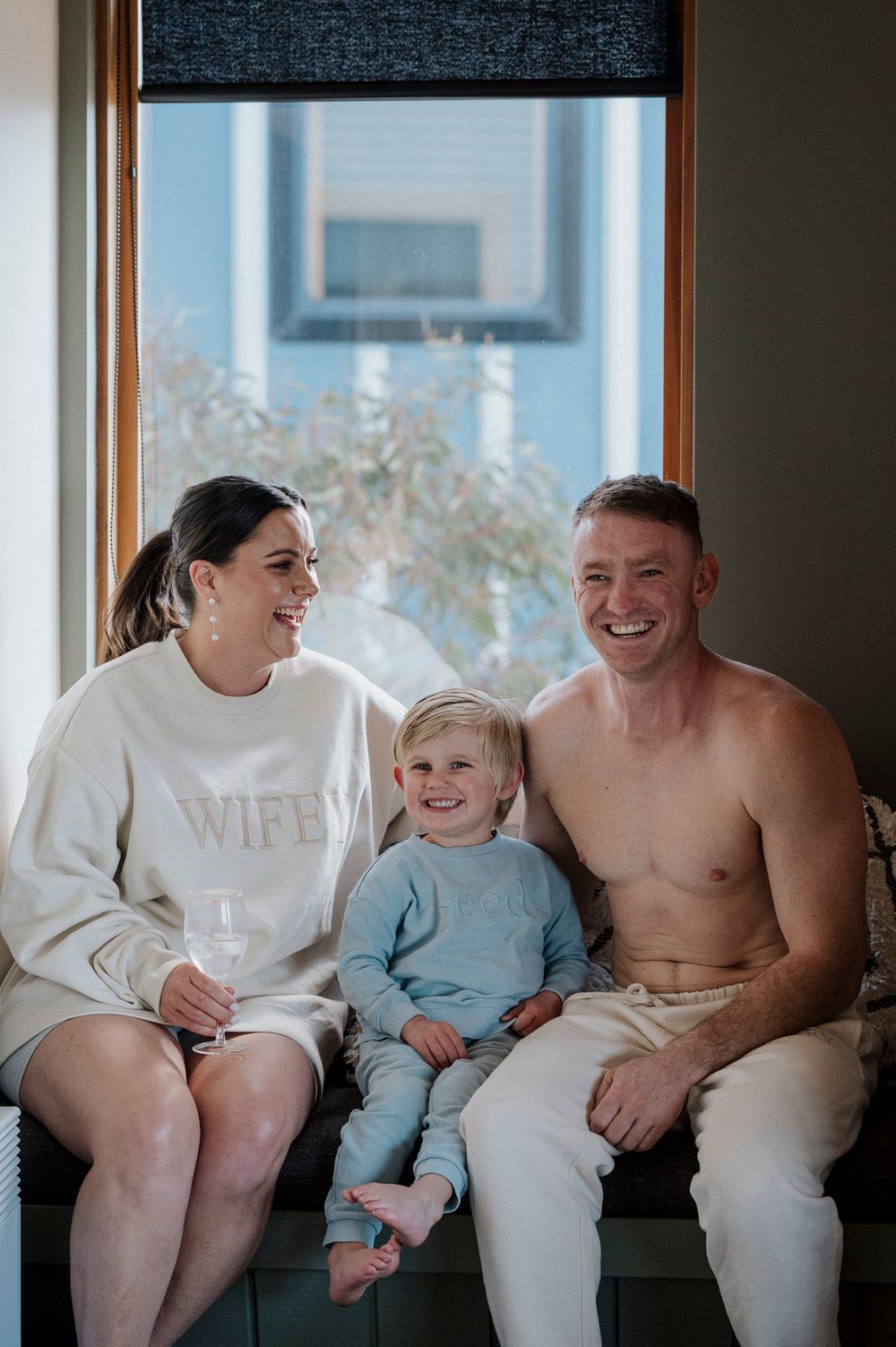 Family in matching white outfits share candid moments while sitting together on a couch.