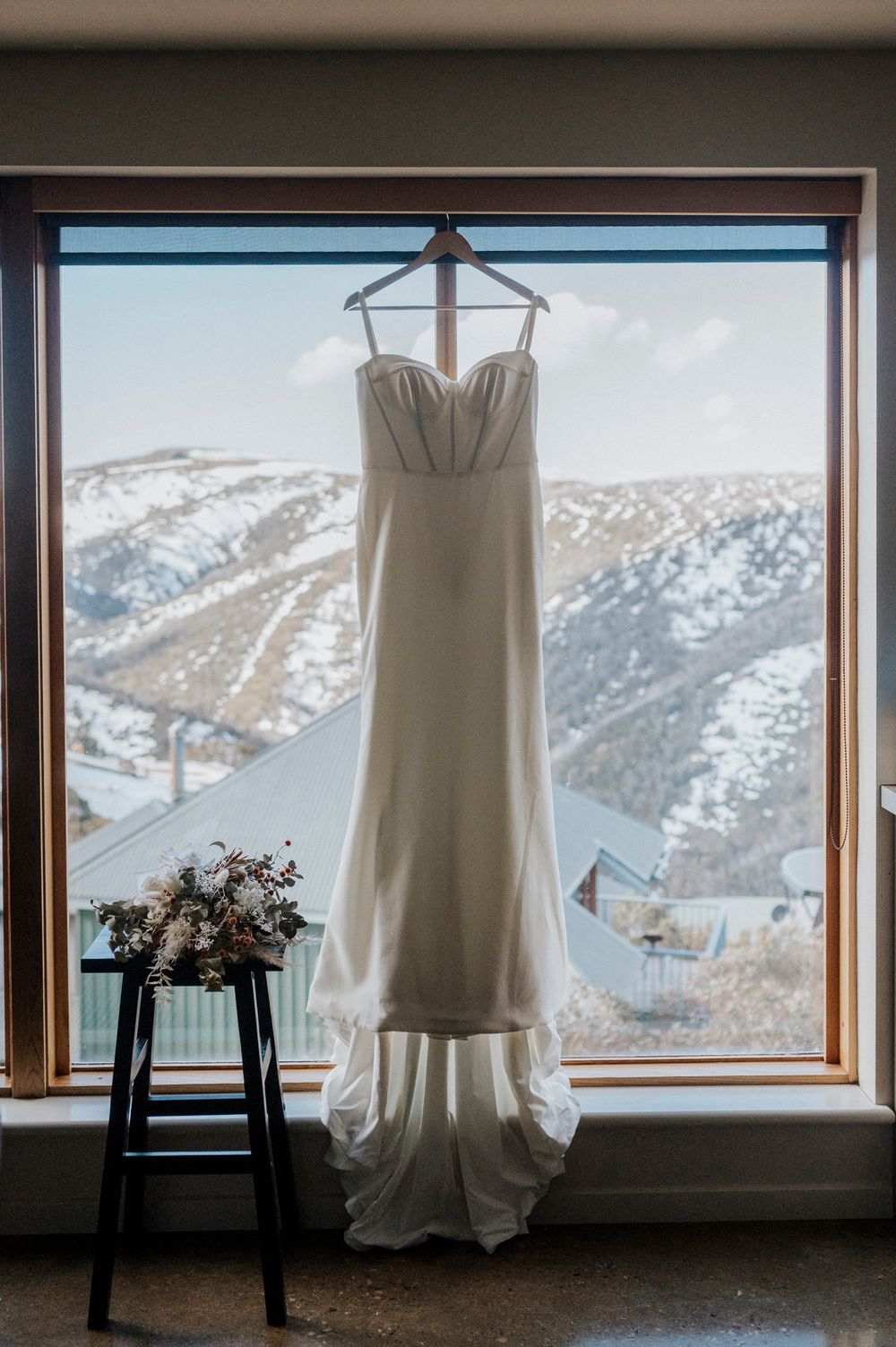 Wedding dress hanging in window frames with snowy mountain landscape views behind.
