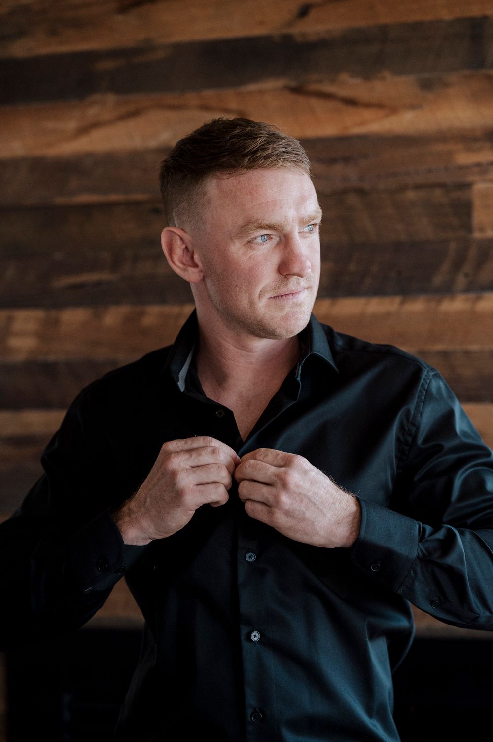 A person wearing a dark button-up shirt adjusts their collar in a series of photos against a rustic wooden background.