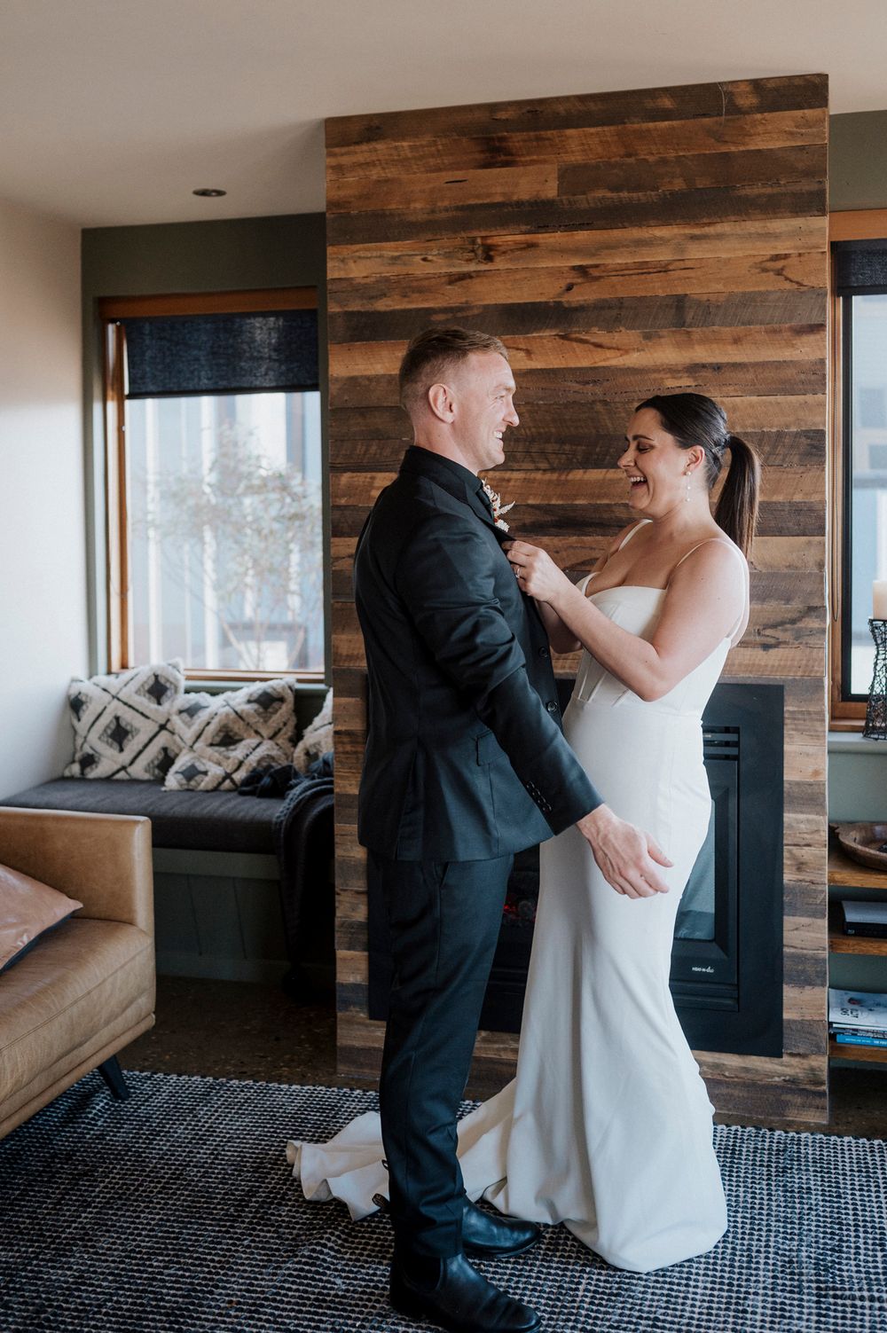 A couple shares an intimate moment before their wedding ceremony against a rustic wooden wall in a modern room.