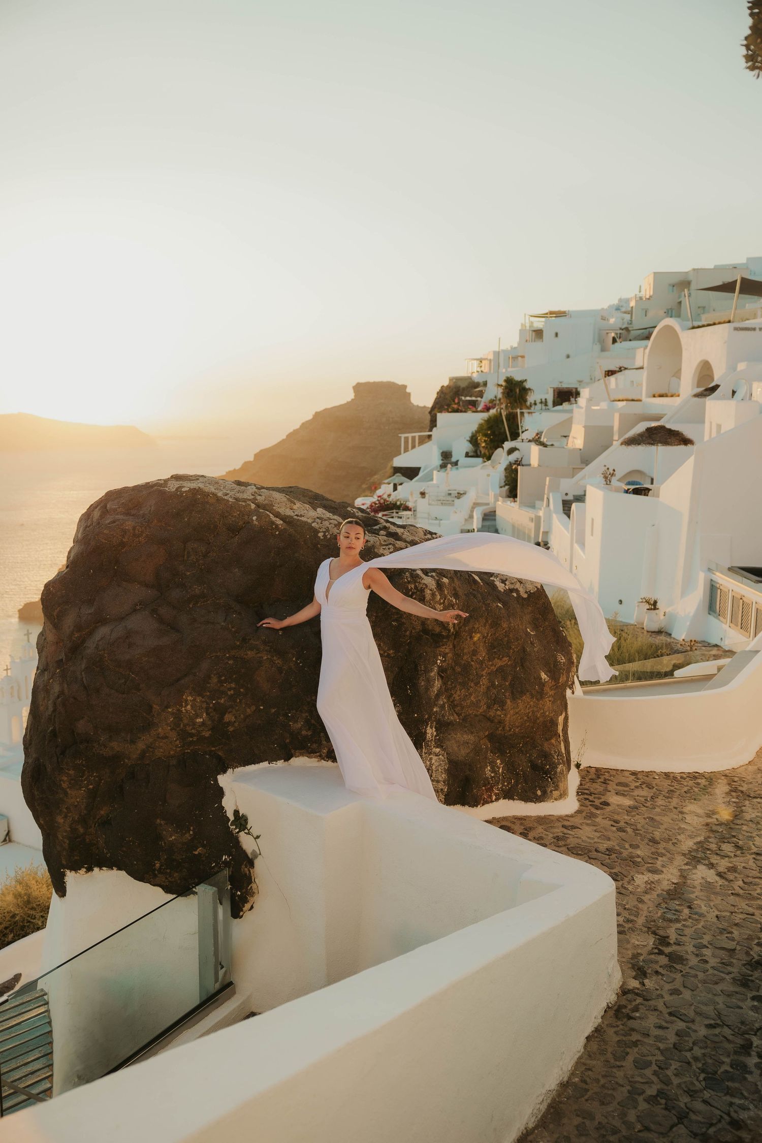 White architectural buildings and pathways of Santorini, Greece at sunset with romantic silhouette against golden light featuring a bride