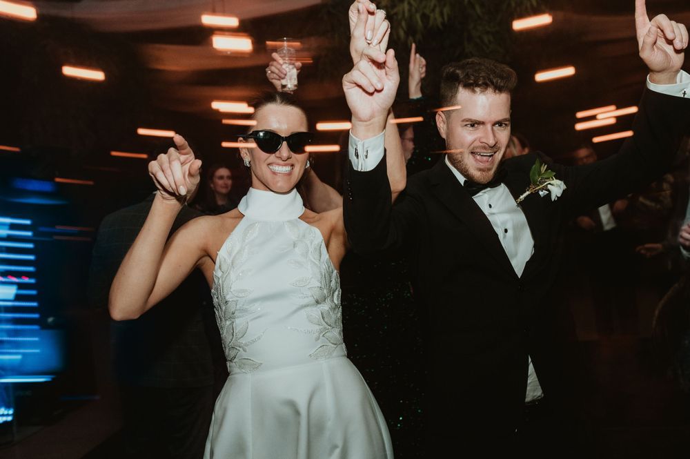 Wedding celebration moment with high energy dancing at a dark reception venue with overhead lighting.