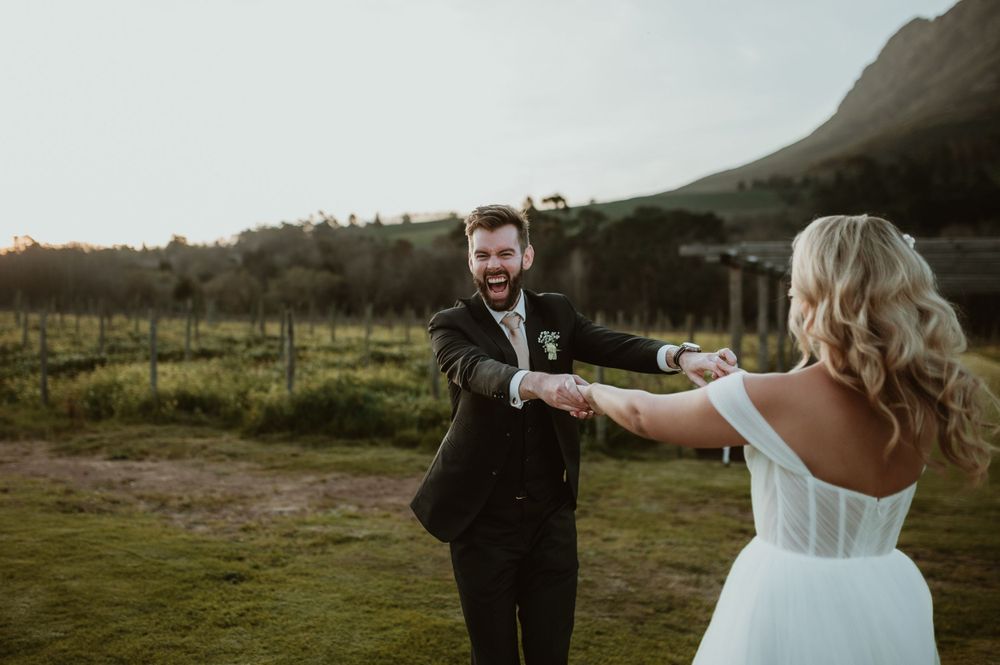 Couple sharing joyful moment during outdoor wedding photoshoot in rustic countryside setting.