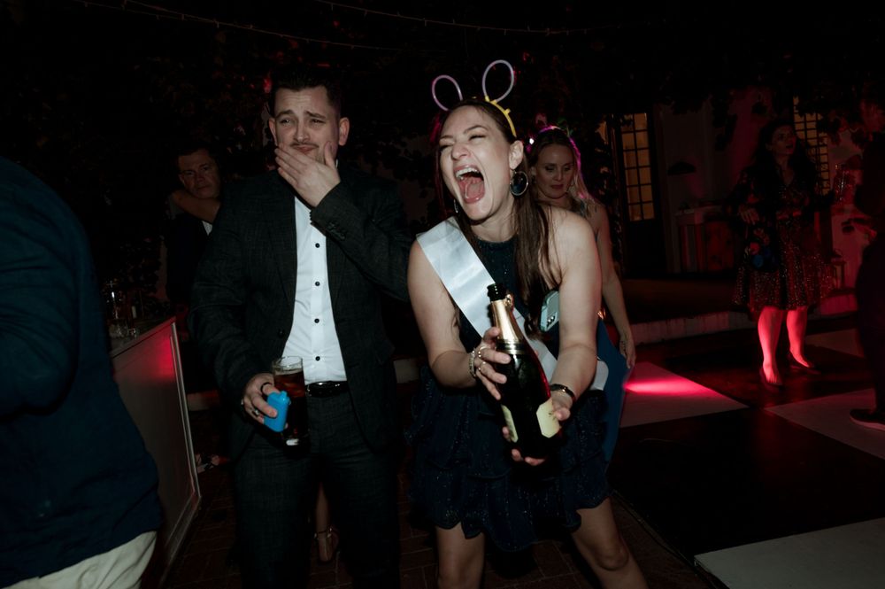 Party guests dance energetically while wearing bunny ears and holding drinks at a dimly lit nighttime event.