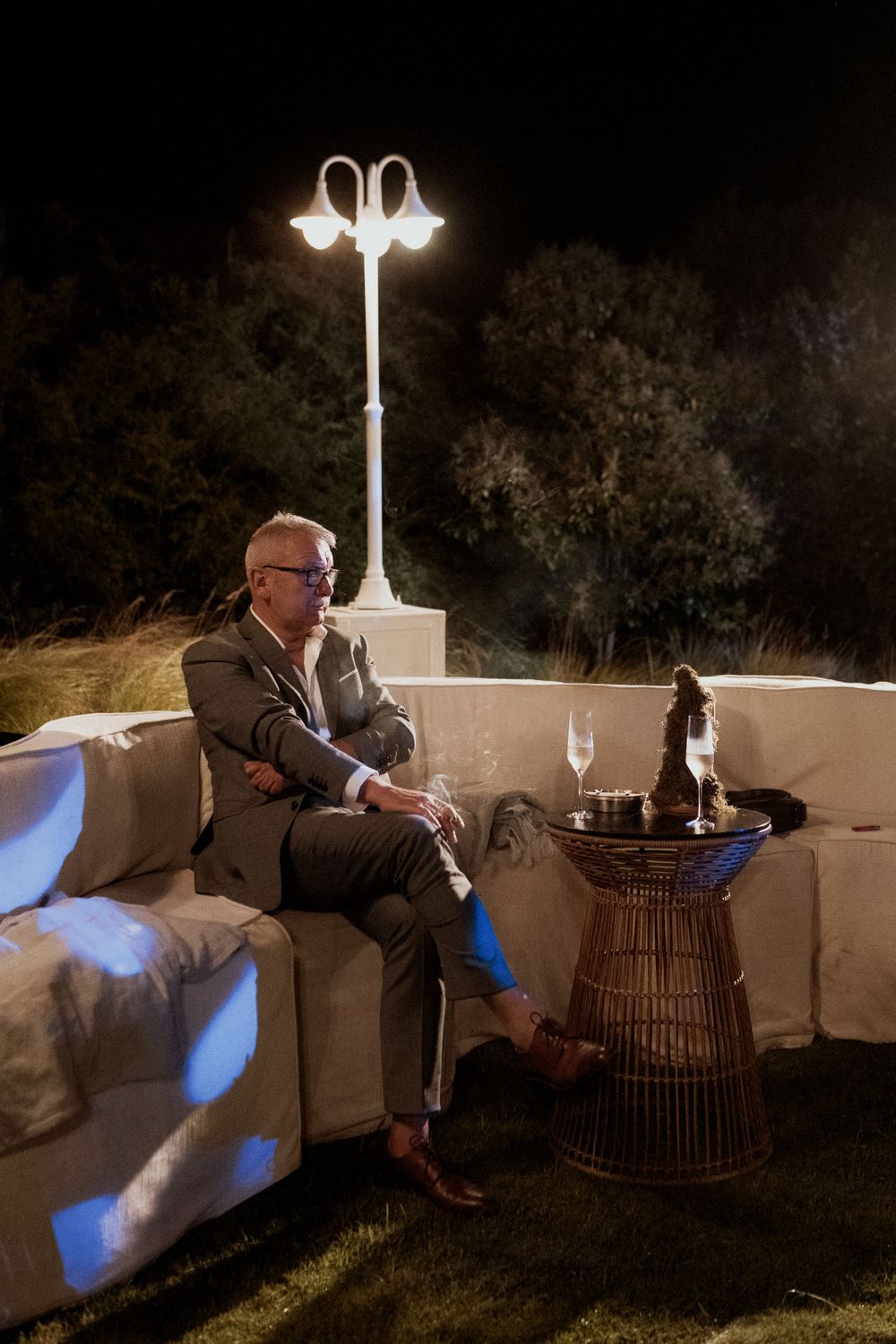 Evening lounge scene with ornate lamp post and person relaxing on outdoor sofa.