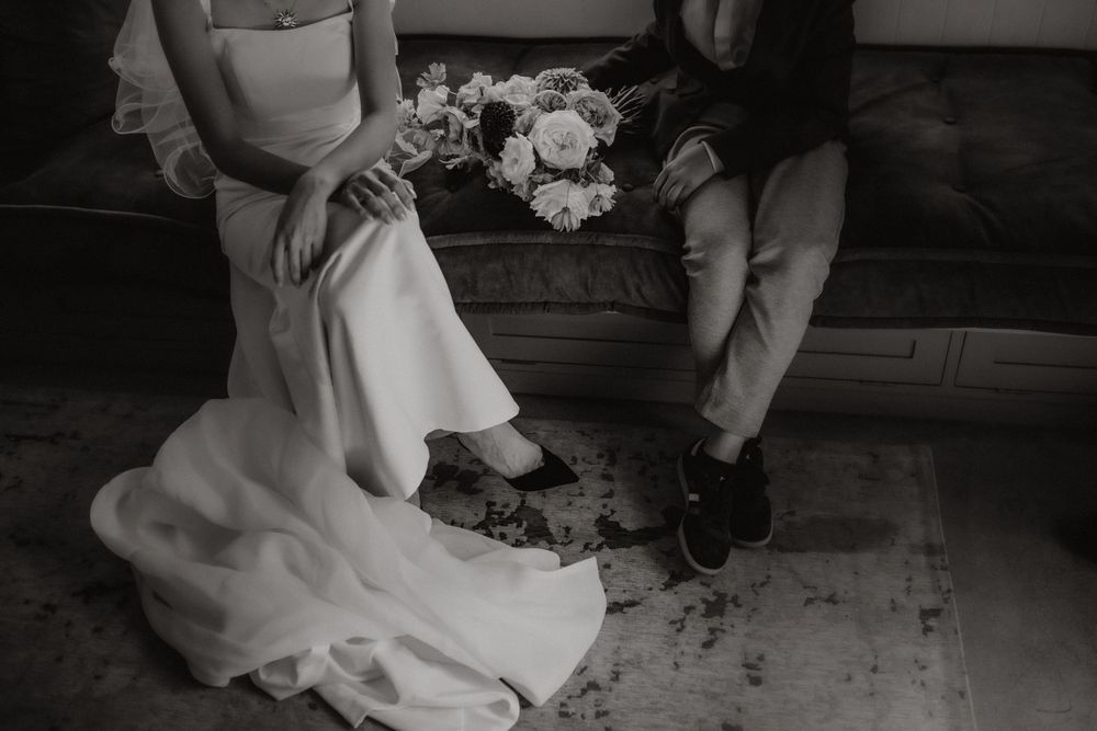 A black and white detail shot of a wedding dress and shoes on a vintage rug.