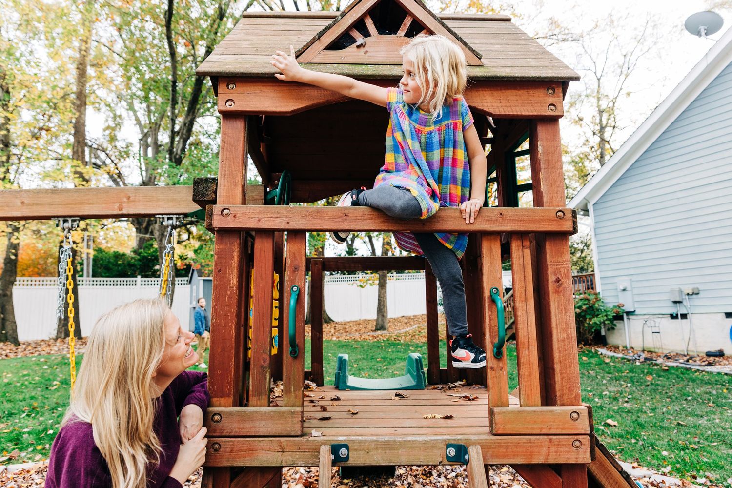 Child plays on a wooden backyard playset swing in the autumn season while wearing cozy fall attire.