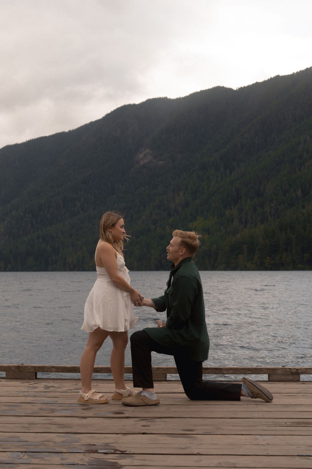 A proposal moment unfolds on a wooden dock overlooking a misty mountain lake.