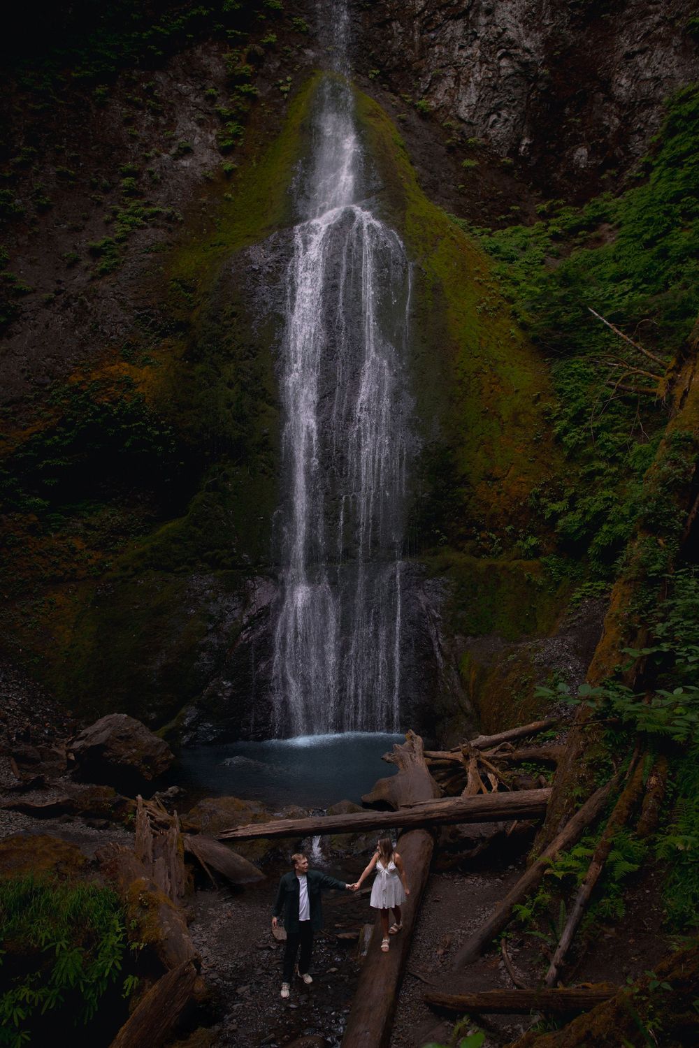 A scenic waterfall cascades down mossy rocks with a wooden bridge crossing in front.