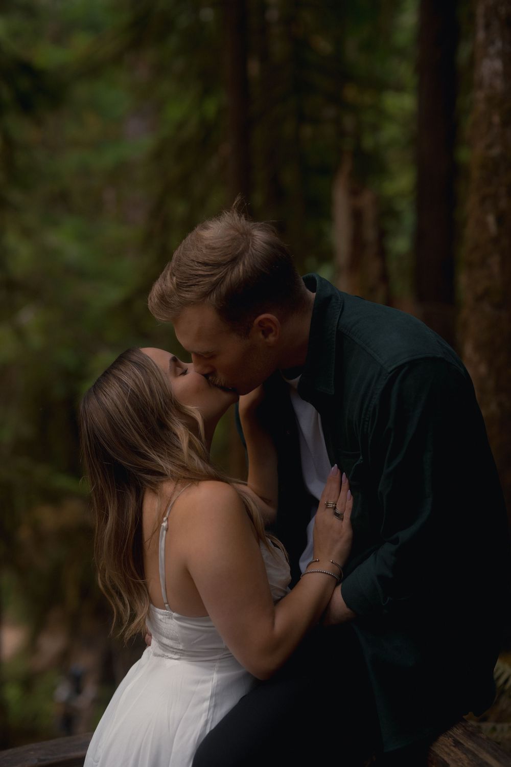 A couple shares an intimate moment together in a forested setting wearing formal attire.