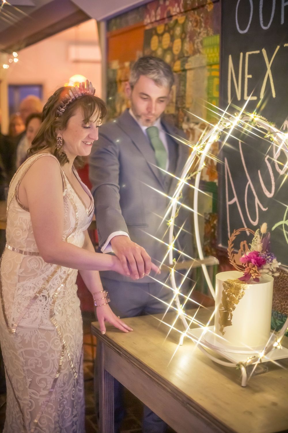 Wedding couple cuts their elegant white tiered cake during reception celebration with sparklers glowing in background.